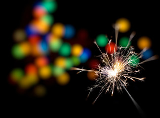Bengal fire is burning against the background of the New Year's multi-colored lights.