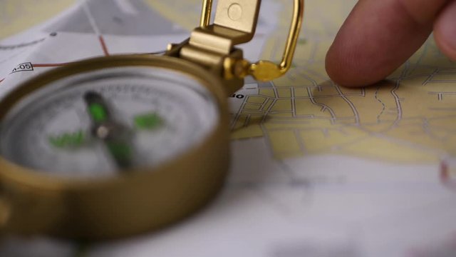 Men's finger planning hiking trip on a map with compass. Finding your way concept