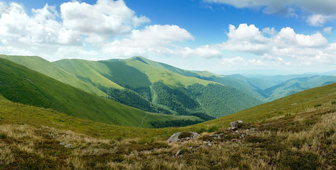 panorama with sunny day on top of green Carpathian mountains range with blue sky and low clouds on top, empty landscape background, high resolution