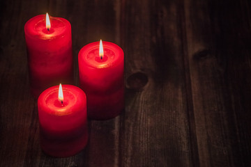 Obraz na płótnie Canvas three red candles with lights on wooden rustic table
