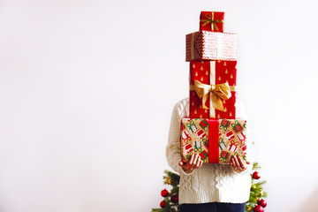 Cropped shot of unrecognizable young woman wearing white knitted sweater, holding big stack of Christmas presents with festive wrapping, tied with golden bow. Isolated background, close up, copy space
