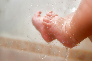 Baby's Feet Under The Shower With Lots Of Drops. Baby's Ankle In The Water. Parents Wash Their Child's Feet Closeup. New Born Caucasian Kid. Newborn Girl Washing After Pool