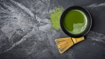 Top view on organic green matcha tea in black ceramic cup with bamboo whisk