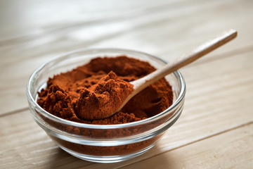 Paprika Powder on wooden spoon, in a glass bowl jar on a wooden table