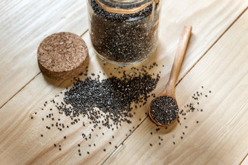 Raw organic black chia seeds on wooden spoon, in a glass bowl jar on a wooden table