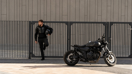 Handsome guy rider with a beard and mustache, stands near the wall of the fence. Bicycle to order...
