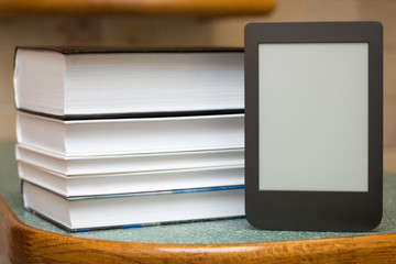 Modern e-book on the background of a stack of thick paper books. Close-up with selective focus. Training and technology concept