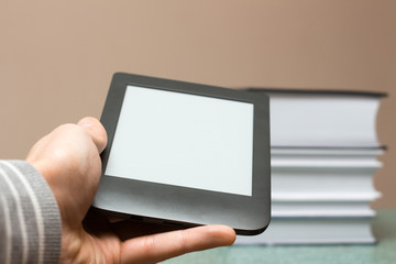 Modern e-book in hand against the background of a stack of thick paper books. Hand holding an e-book. Close-up with selective focus. Training and technology concept