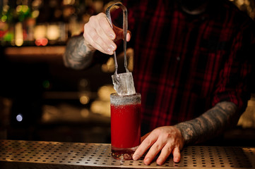 Barman putting big ice cube into a tomato bloody mary cocktail