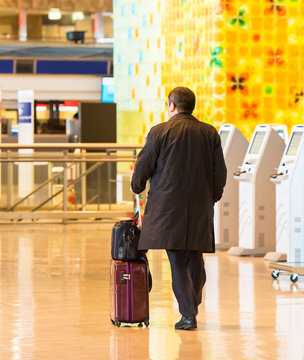 Man in a raincoat with a suitcase at the airport, Tokyo, Japan. Back view. With selective focus.
