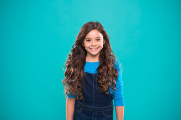 Extreme hair volume. Kid girl long healthy shiny hair. Kid happy cute face with adorable curly hairstyle stand over blue background. Little girl grow long hair. Teaching healthy hair care habits