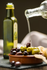 Green and dark olives on a brown greek plate. Olive oil.