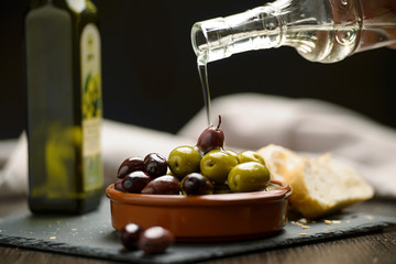 Green and dark olives on a brown greek plate. Olive oil.