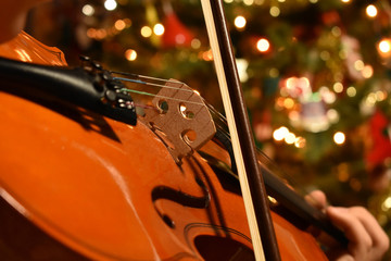 a young person playing the violin with a Chrismas tree in the background © Blessings Captured