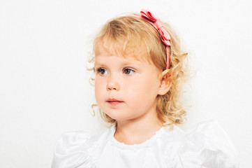 Studio shot of adorable 3 year old toddler girl with blonde curly hair, looking away