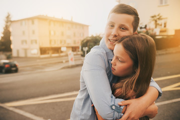 Outdoor portrait of happy boy and girl, brother hugging little sister