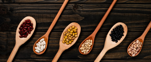 Diversity of beans inside wooden spoons. Black wood background.