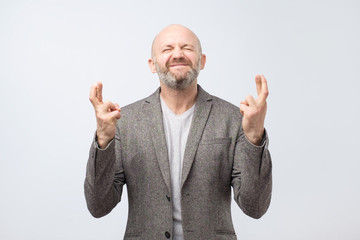 Optimistic mature man win suit crosses his fingers making a wish.