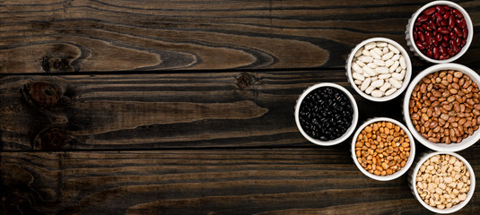 Assortment of beans in a pot. Wooden black background.