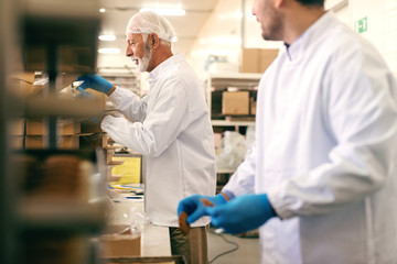 Two colleagues packing cookies in boxes while standing in food factory.
