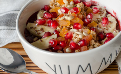 Smoothie acai bowl topped with pomegranate, bananas, flaxseeds, cedar seeds, dried apricot and granola. Acai breakfast superfoods smoothie bowl and spoon. close up, angle view