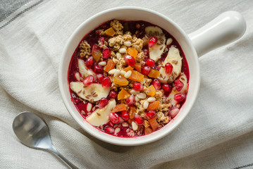 Smoothie acai bowl topped with pomegranate, bananas, flaxseeds, cedar seeds, dried apricot and granola. Acai breakfast superfoods smoothie bowl and spoon. Overhead, top view.
