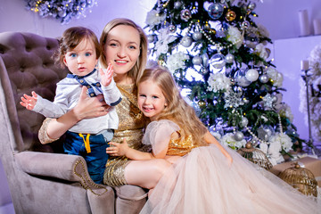 Happy family mother, son and daughter in luxurious dresses near Christmas tree. Family look. Happy New Year and Christmas theme. Festive mood
