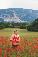 Fototapeta na wymiar Beautiful woman with blond hair enjoying amazing view of poppy field, wearing red dress. Image taken in Geneva, Switzerland