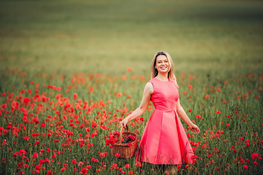 Beautiful woman with blond hair enjoying amazing view of poppy field, wearing pink dress. Image taken in Geneva, Switzerland