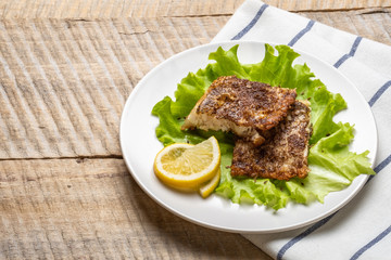 Two pieces of grilled fish fillet with the fresh leafs of lettuce and lemon on old wooden background. Top view.