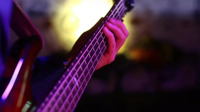 musician plays bass guitar in discolights. hands on the fingerboard