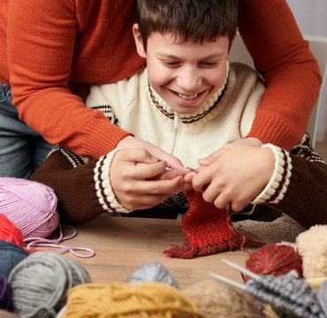 Mother is learning her child boy to knit. Colorful wool yarns are on the wooden table.