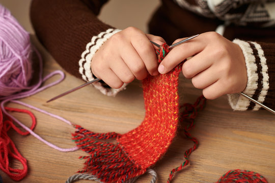 Child boy is learning to knit. Colorful wool yarns are on the wooden table. Hand closeup.