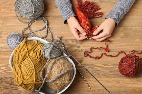 Child girl is learning to knit. Colorful wool yarns are on the wooden table. Hand closeup.