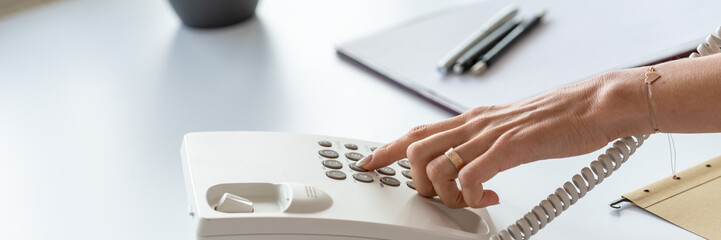 Wide view image of hand of a secretary dialing a telephone number - obrazy, fototapety, plakaty