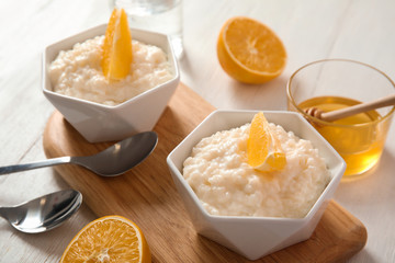 Creamy rice pudding with orange slices in bowls served on wooden table