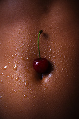 The belly of a dark-skinned woman with cherries and drops of water. Sexy girl closeup. African American pretty girl. Cherry for dessert. Erotic concept.