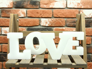 Love - białe litery na drewnianym regale w tle ceglana ściana