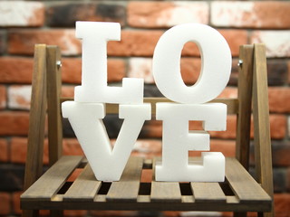 Love - białe litery tworzące napis miłość na drewnianym regale na tle ceglanej ściany