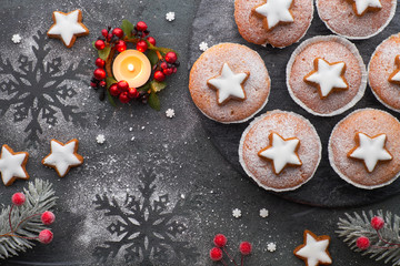 Obraz na płótnie Canvas Top view of the wooden board with sugar-sprinkled muffins and Christmas star cookies on dark with candle