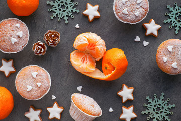 Fototapeta na wymiar Top view of the table with satsumas, sugar-sprinkled muffins and Christmas star cookies on dark