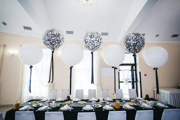 Festive dinner table decor. White and black balloons hang over the restaurant table served with...