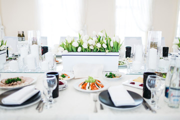 Dinner table serving. White tulips stand in flowerpots on white table served with delicious food