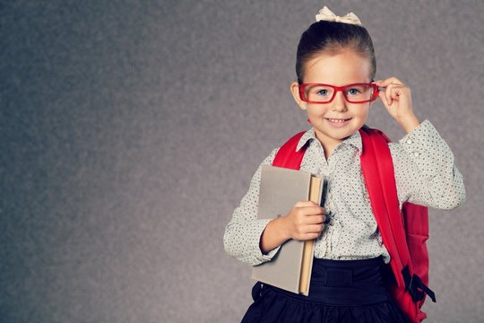 Cute little schoolgirl in glasses on library background
