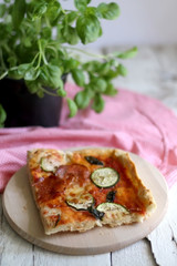 Slice of homemade pizza with tomato sauce, cheese, salami and zucchini. Fresh basil in the background. Selective focus.