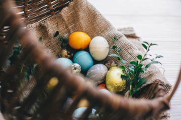 Stylish easter eggs on cloth in rustic basket on white wooden background. Easter hunt concept....