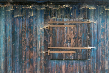 schöne grunge blaue Holz Bretterwand eines alten Schuppens mit verschlossenem Fenster mit rustikaler Holzmaserung und vielen Spinnennetzen