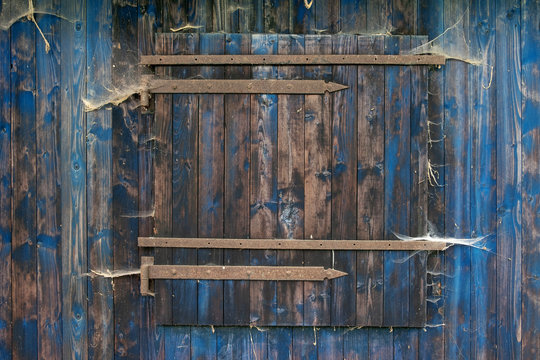 blaue Holz Bretterwand enes rustikalen Schuppens grunge mit verschlossenem Fenster mit rustikaler Holzmaserung und vielen Spinnennetzen