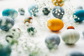 Stylish easter eggs with spring flowers on white wooden background. Modern easter eggs painted with natural dye in blue, grey, yellow marble color. Happy Easter, greeting card