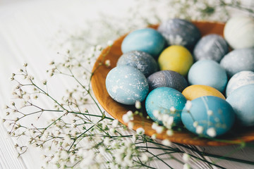 Stylish easter eggs with spring flowers on wooden plate on white wooden background. Modern easter...